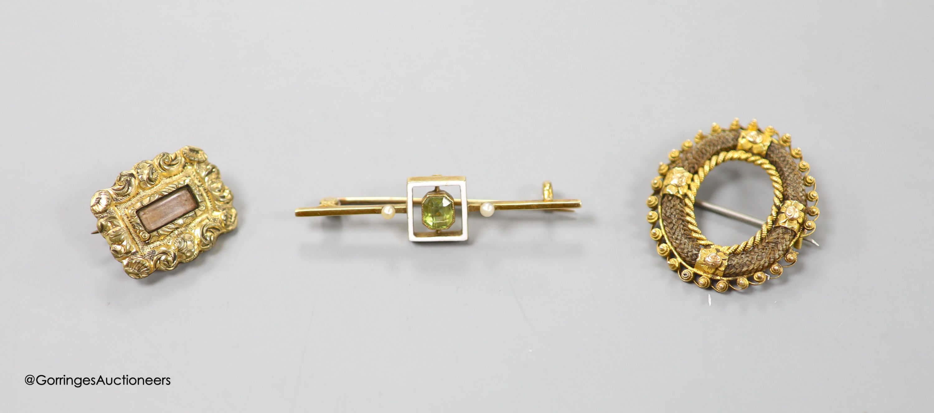 A George III gold plated mourning brooch, 20mm, a 19th century yellow metal and plaited hair openwork brooch, and an early 20th century yellow metal, peridot, seed pearl and white enamel set bar brooch, 42mm, gross 2.8 g